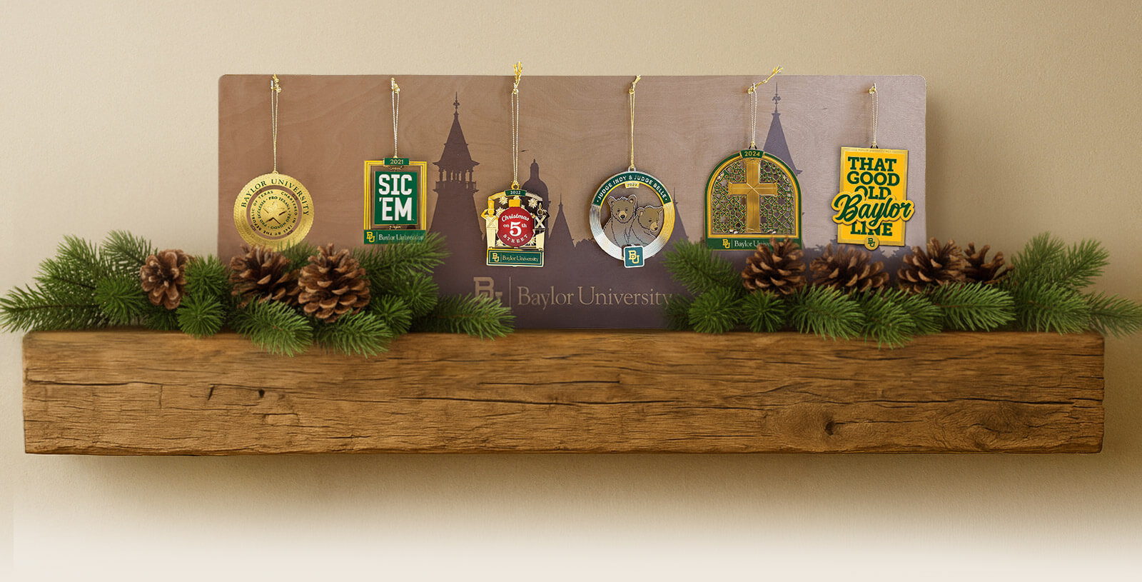 A collection of 6 Baylor traditions ornaments on a wood display hanger sitting on a wood mantle with pine branches and pinecone decorations